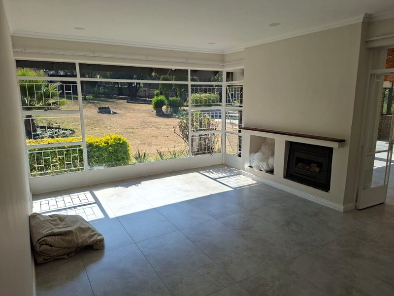 Bright and spacious living area featuring large steel-framed windows with garden views, tiled flooring, and a built-in fireplace.