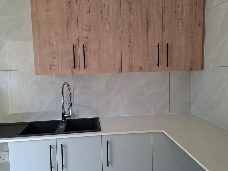 Modern kitchen area featuring light grey lower cabinets, wood-grain upper cabinetry, stone countertops, and a contemporary double basin sink with a gooseneck faucet.