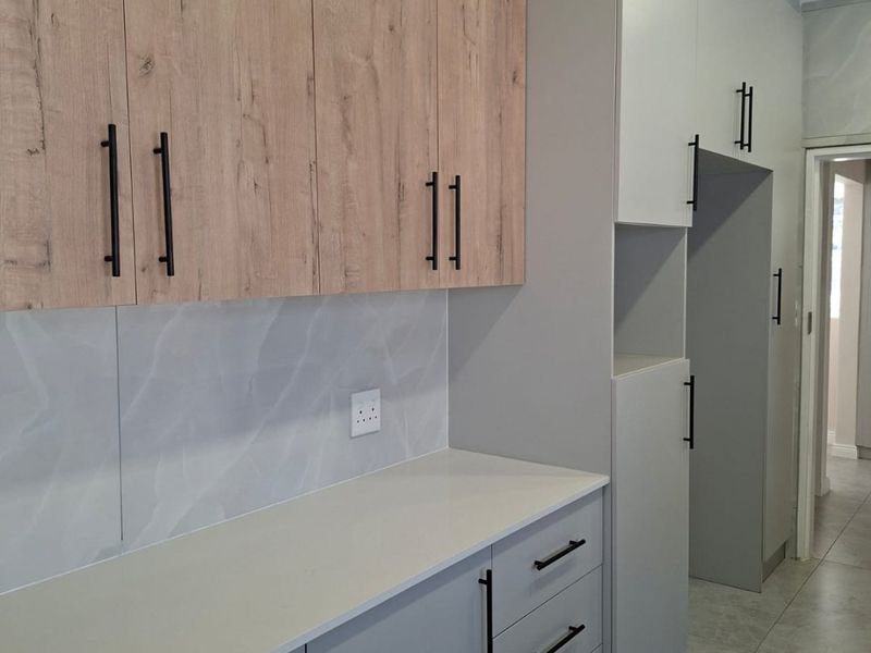 Modern kitchen featuring light wood-look upper cabinets, grey lower cabinetry, stone countertops, and a sleek tiled backsplash in a clean, contemporary design.