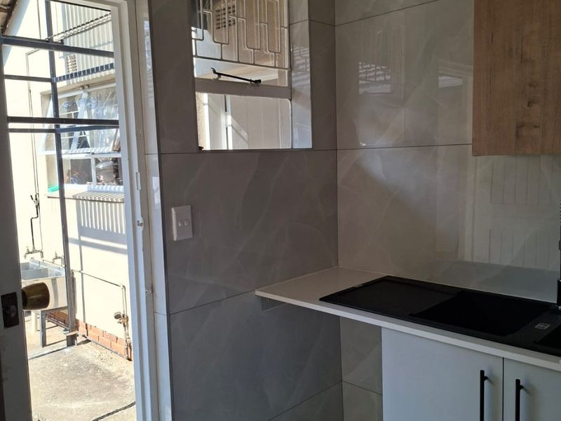 A modern, clean scullery area featuring sleek cabinetry, stone countertops, and a tiled splashback, with direct access to the exterior.