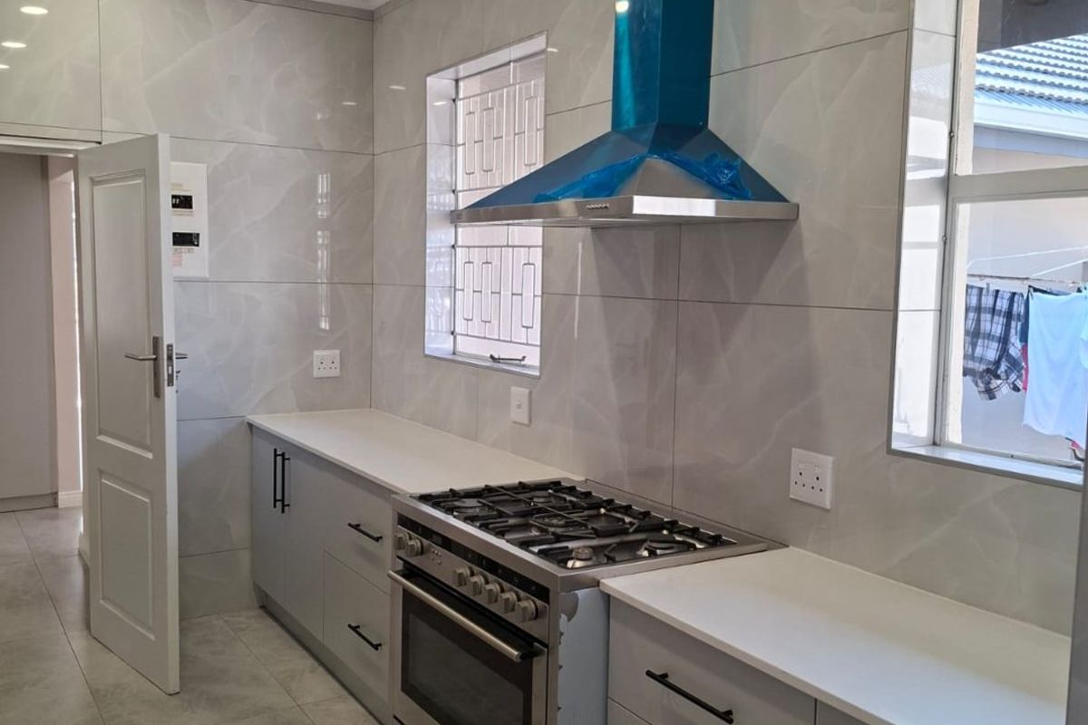 Modern kitchen featuring sleek grey cabinetry, stone-look wall tiles, gas stove with extractor fan, and recessed lighting in a clean, contemporary finish.