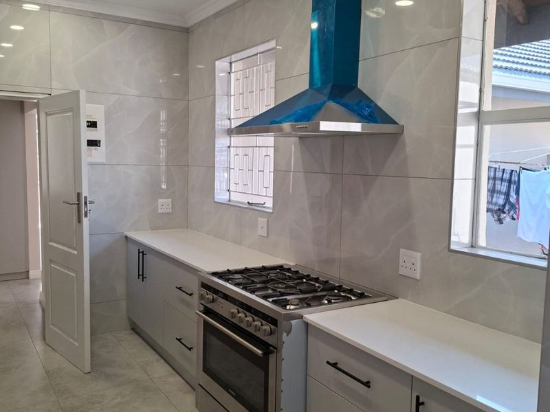 Modern kitchen featuring sleek grey cabinetry, stone-look wall tiles, gas stove with extractor fan, and recessed lighting in a clean, contemporary finish.