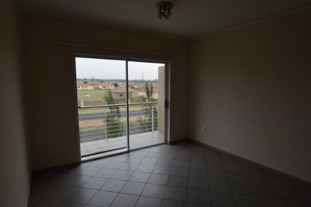 An empty living room featuring tiled flooring and a sliding glass door that provides access to a balcony with an exterior view.