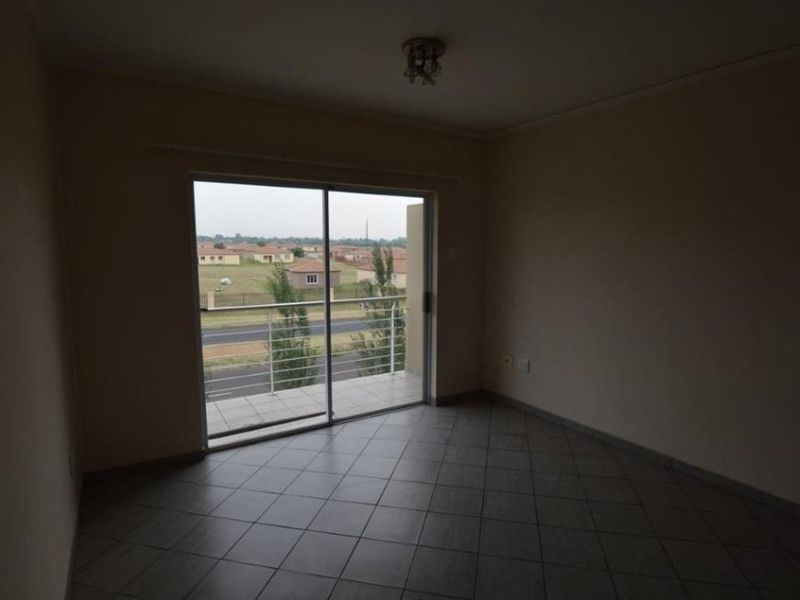 An empty living room featuring tiled flooring and a sliding glass door that provides access to a balcony with an exterior view.