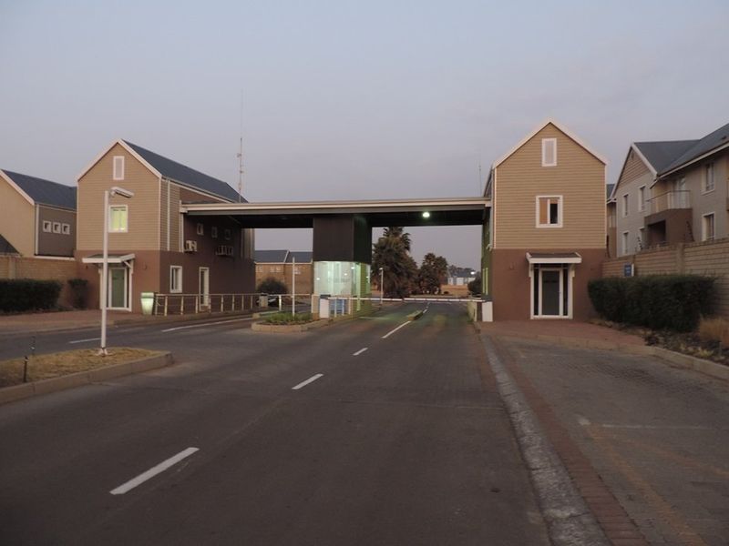 The entrance to the apartment complex features a secure gatehouse with boom gate access and paved driveway infrastructure.