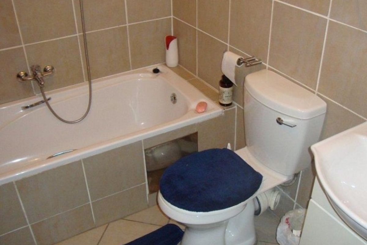 A functional bathroom featuring a bathtub with shower mixer, toilet, and vanity basin, finished with neutral wall and floor tiling.