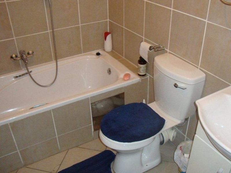 A functional bathroom featuring a bathtub with shower mixer, toilet, and vanity basin, finished with neutral wall and floor tiling.