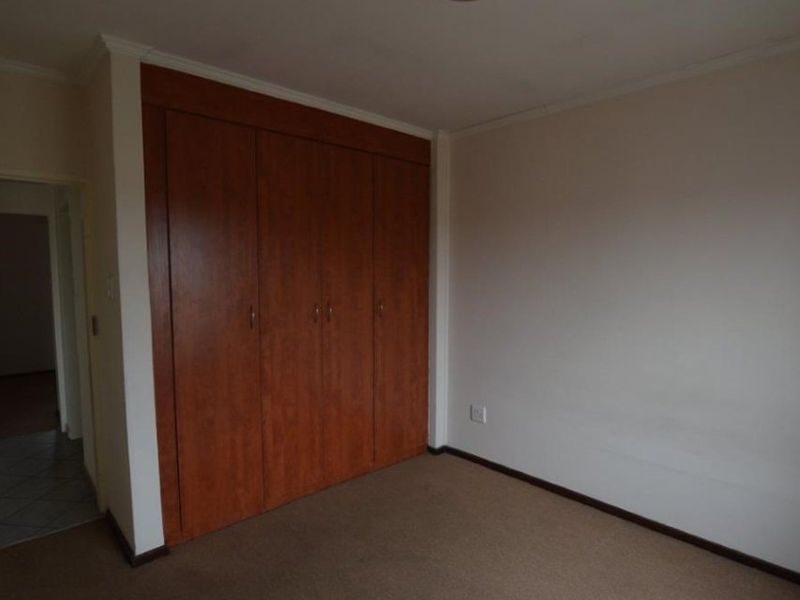 A vacant bedroom featuring neutral walls, carpeted flooring, and floor-to-ceiling built-in wooden cupboards.