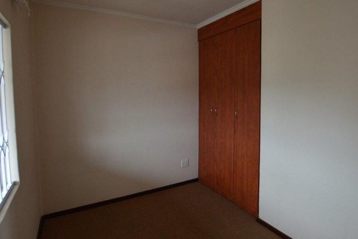 A vacant bedroom featuring neutral walls, carpet flooring, and a built-in wooden wardrobe.