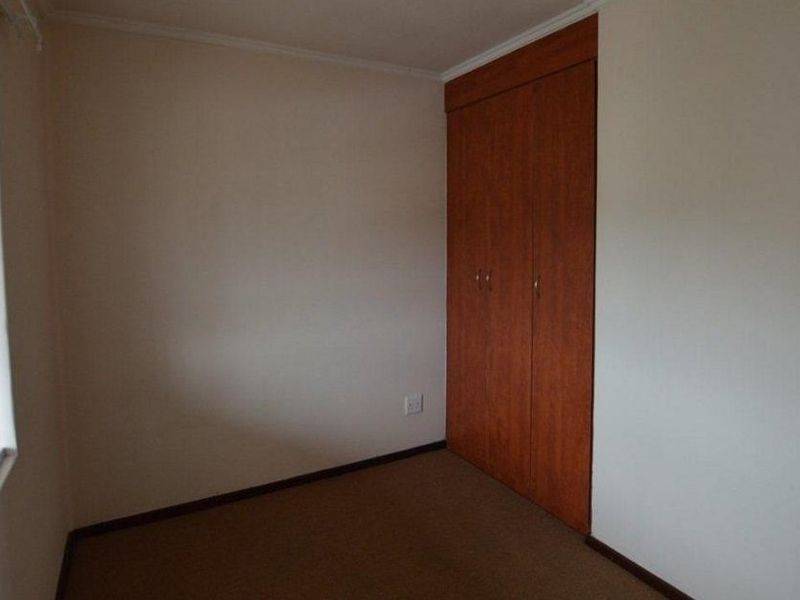 A vacant bedroom featuring neutral walls, carpet flooring, and a built-in wooden wardrobe.