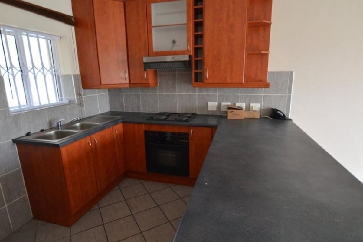 A functional kitchen featuring wooden cabinetry, dark laminate countertops, a built-in oven and hob, and tiled finishes throughout.