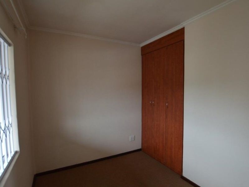 A simple, empty bedroom featuring neutral walls, carpeted flooring, and a built-in wooden wardrobe.