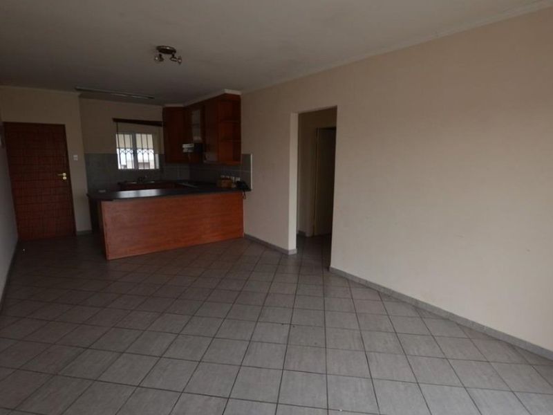 An open-plan living and kitchen area featuring tiled flooring, built-in wooden cabinetry, and a breakfast bar, presenting a blank canvas for renovation.