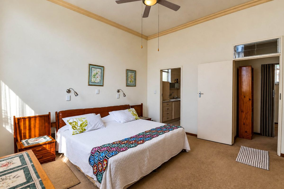 A spacious bedroom featuring carpeted flooring, a ceiling fan, and decorative coving, with an adjoining room visible through the doorway.