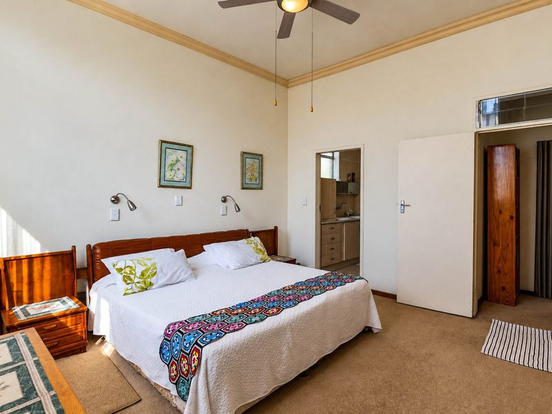 A spacious bedroom featuring carpeted flooring, a ceiling fan, and decorative coving, with an adjoining room visible through the doorway.