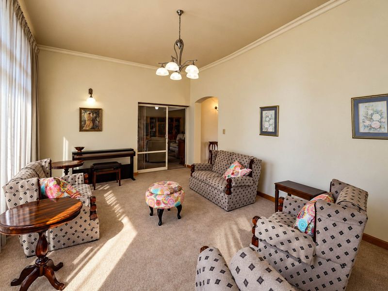 A spacious living room featuring neutral carpeting, a classic chandelier, and an arched doorway leading to an adjacent room.