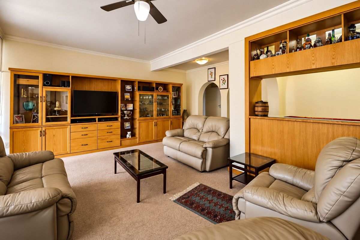 Spacious living room featuring extensive built-in wooden cabinetry, a ceiling fan, and a dedicated built-in bar area with an arched entryway.