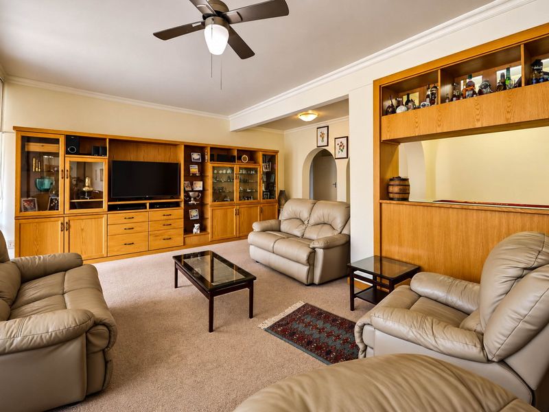 Spacious living room featuring extensive built-in wooden cabinetry, a ceiling fan, and a dedicated built-in bar area with an arched entryway.