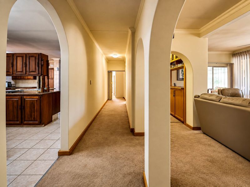 A central hallway featuring classic arched doorways, connecting the kitchen and living areas with neutral carpeting and traditional architectural detailing.
