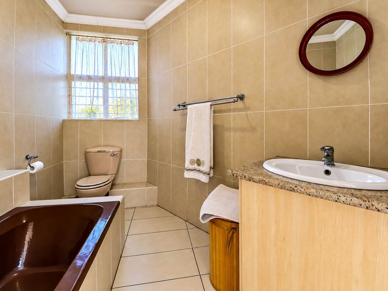 A functional bathroom featuring a built-in vanity with granite countertop, a drop-in basin, a bathtub, and a toilet, finished with neutral wall and floor tiles.