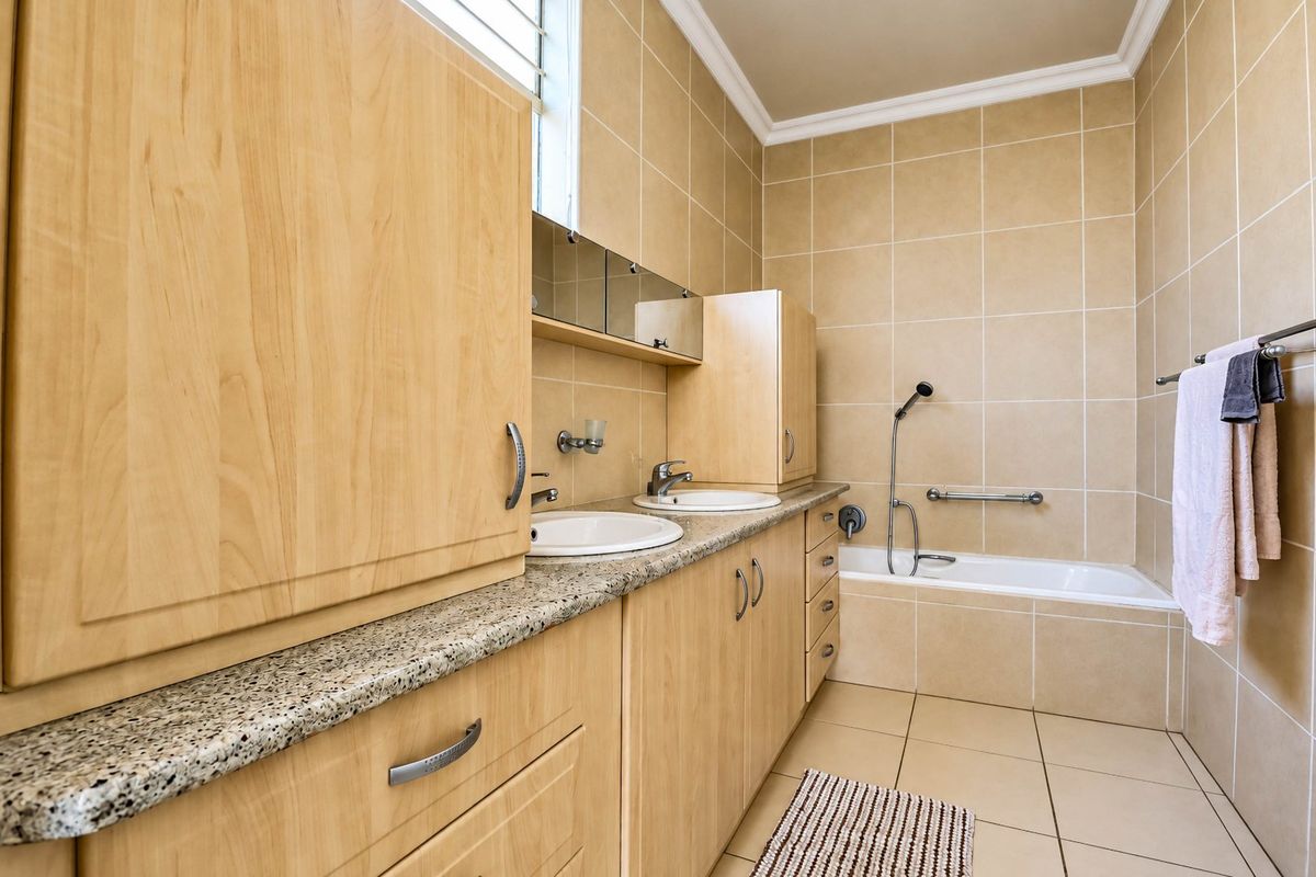 A functional bathroom featuring a double vanity with granite countertops, built-in light wood cabinetry, and a tiled bathtub area with a handheld shower fixture.