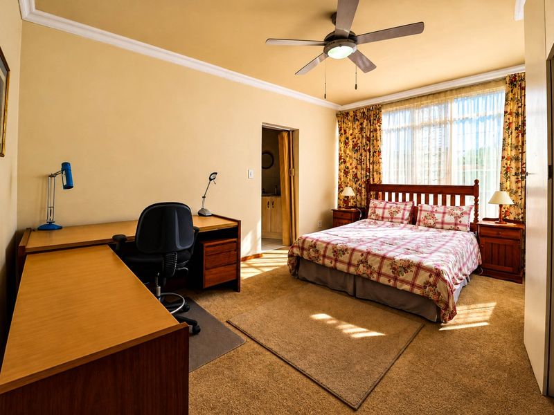 Spacious bedroom featuring carpet flooring, a ceiling fan, crown molding, and an integrated desk area with direct access to an en-suite bathroom.