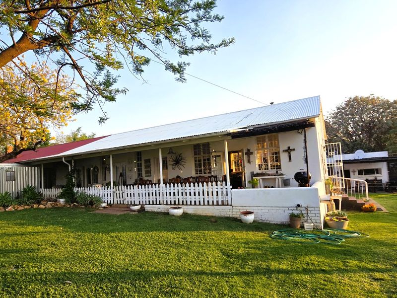 Rear view of a charming cottage-style house featuring a covered veranda, white picket fencing, and a spacious garden area.