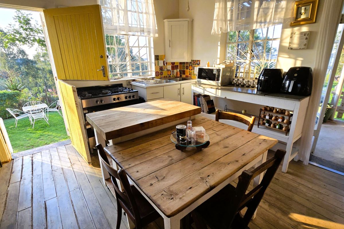 A rustic kitchen featuring timber flooring, a gas stove, and a dutch door opening directly onto a garden patio area.