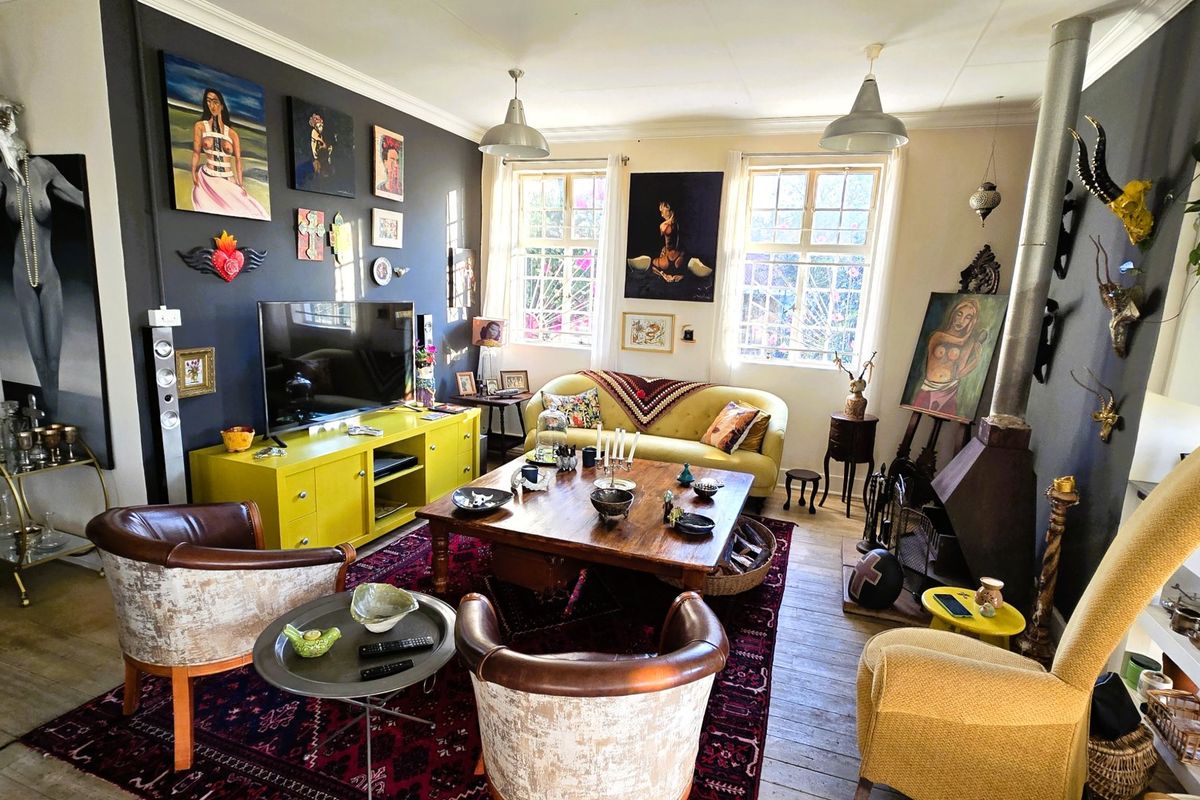 A characterful living room featuring timber flooring, a freestanding fireplace, and large multi-pane windows that provide ample natural light.