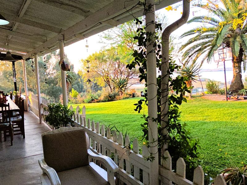 A covered outdoor patio overlooking a lush green garden, featuring a picket fence boundary and views of the surrounding landscape.