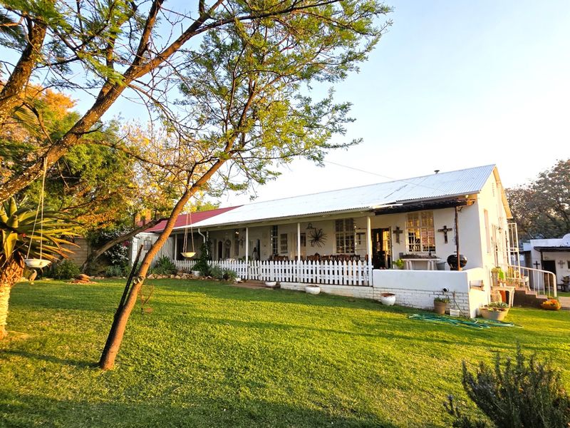 Rear view of a single-story house featuring a covered patio, corrugated metal roof, and a well-maintained garden area.