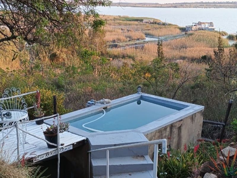 An elevated concrete swimming pool overlooking a natural landscape and water view, featuring a small deck area and metal safety railings.