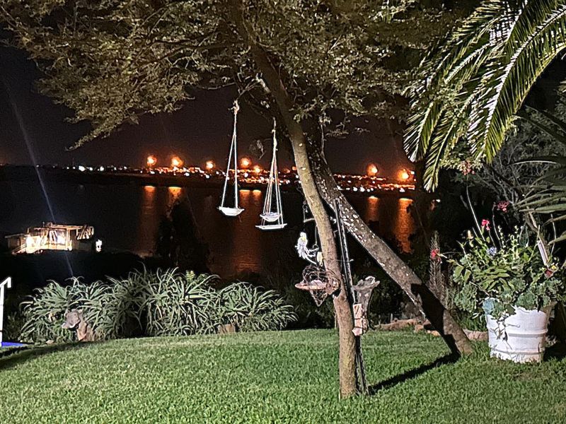 Night view of the waterfront and distant city lights from the property garden, featuring mature trees and landscaped lawn.