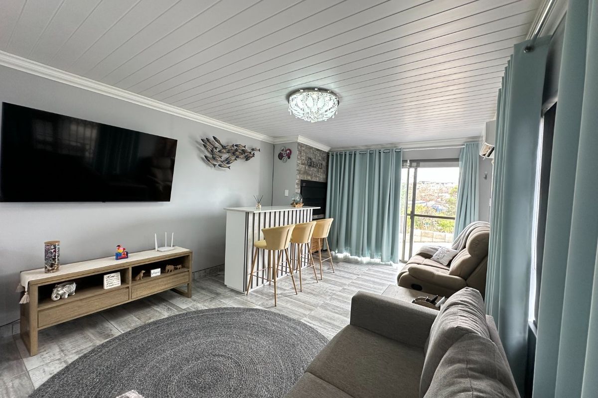 A well-maintained living room featuring a stone accent wall, built-in bar, tongue and groove ceiling, and direct access to an outdoor balcony.