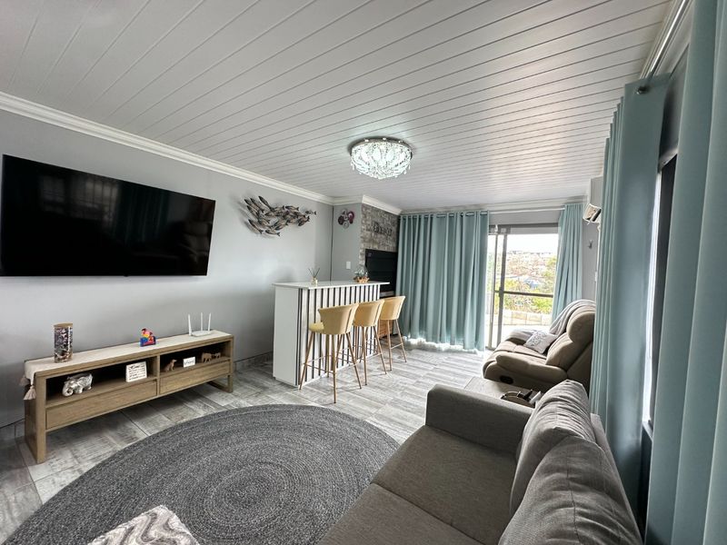A well-maintained living room featuring a stone accent wall, built-in bar, tongue and groove ceiling, and direct access to an outdoor balcony.