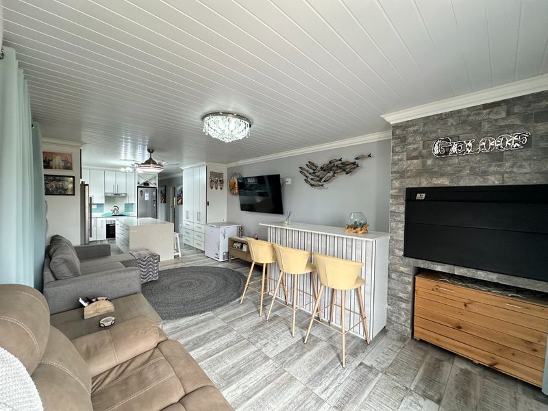 Spacious open-plan living area featuring a modern kitchen with island, a stone-clad fireplace, and a built-in bar, finished with tiled floors and tongue-and-groove ceilings.