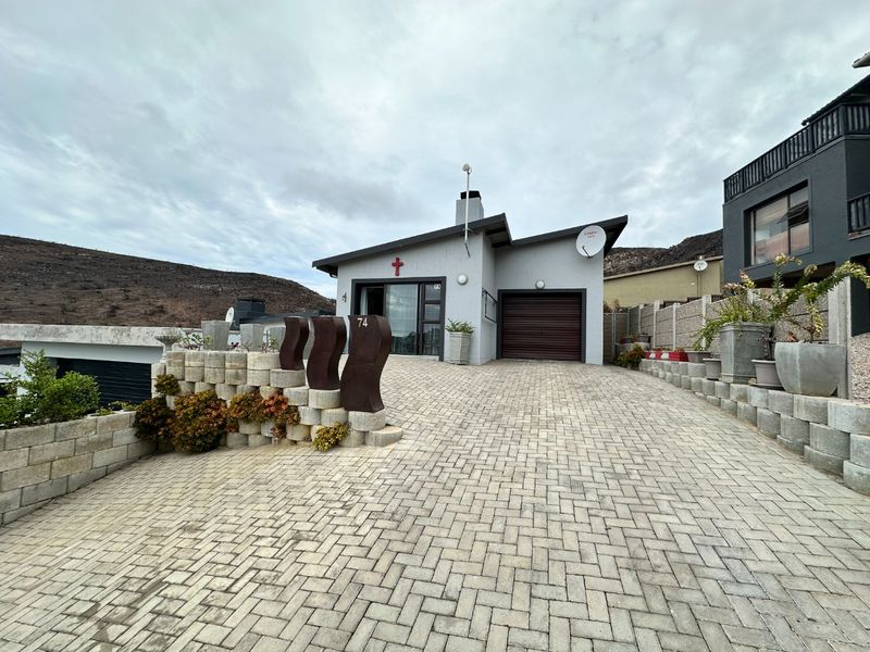 Front view of the property featuring a paved driveway, retaining wall, and integrated garage.