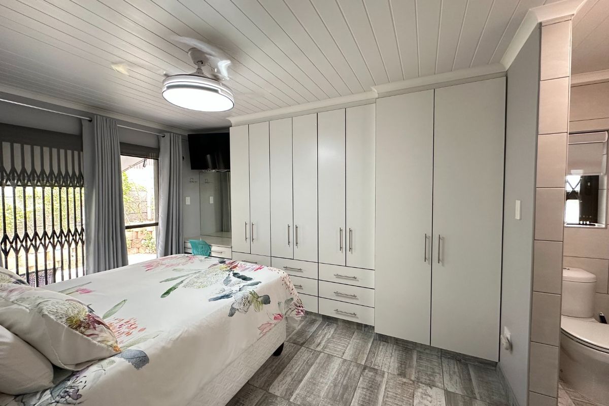 A well-maintained bedroom featuring built-in cupboards, a tongue and groove ceiling with a fan, tiled flooring, and an en-suite toilet.