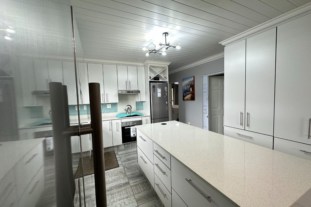 Modern kitchen featuring white cabinetry, a large central island with stone countertops, tiled flooring, and a distinctive tongue and groove ceiling.