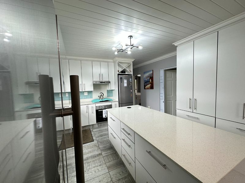 Modern kitchen featuring white cabinetry, a large central island with stone countertops, tiled flooring, and a distinctive tongue and groove ceiling.