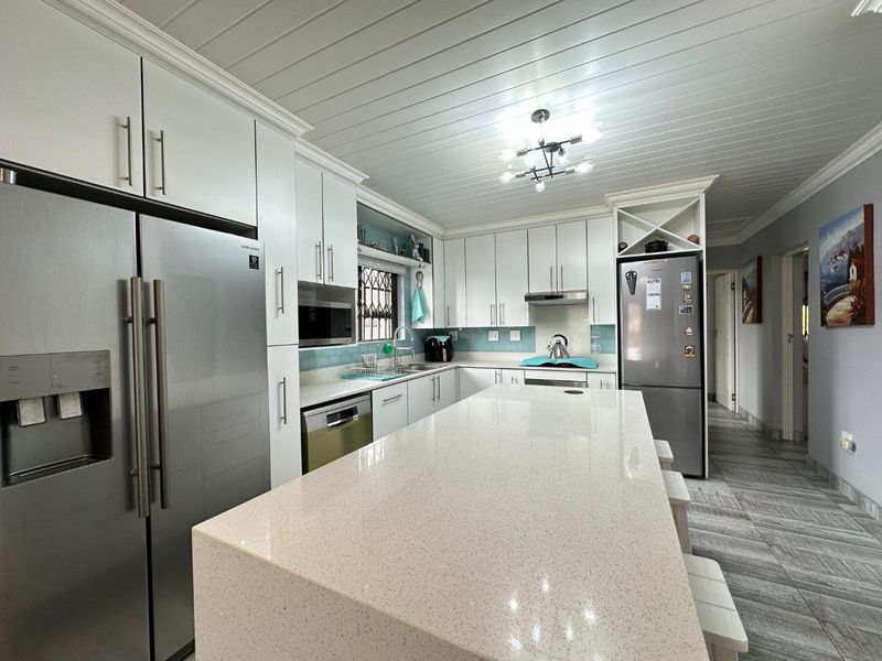 Modern kitchen featuring a large quartz island, white cabinetry, tiled backsplash, and a distinctive tongue and groove ceiling with contemporary lighting.