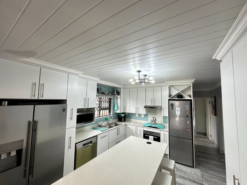 Modern kitchen featuring white cabinetry, stone countertops, integrated appliances, and a distinctive tongue and groove ceiling with a central light fixture.