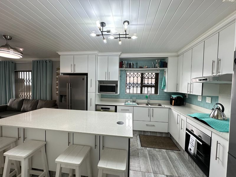 Modern open-plan kitchen featuring white cabinetry, quartz countertops, a central island, and integrated appliances, seamlessly flowing into the adjacent living area.