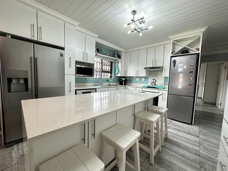 Modern kitchen featuring white cabinetry, quartz countertops, a central island, subway tile backsplash, and contemporary lighting fixtures.