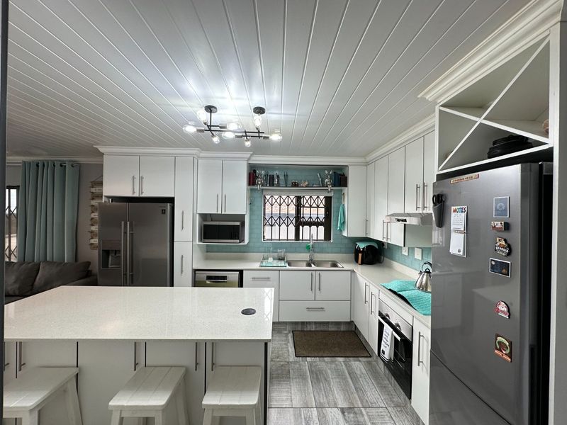 Modern kitchen featuring white cabinetry, quartz countertops, a central island, and a tiled backsplash, complemented by a stylish tongue and groove ceiling.