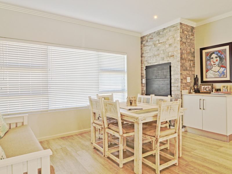 A bright dining area featuring a rustic brick fireplace, built-in cabinetry, and large windows with venetian blinds, finished with modern laminate flooring.