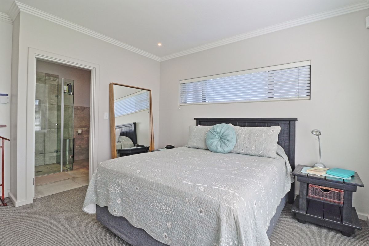 A well-maintained bedroom featuring neutral walls, carpeted flooring, recessed lighting, and an adjoining en-suite bathroom with a glass-enclosed shower.