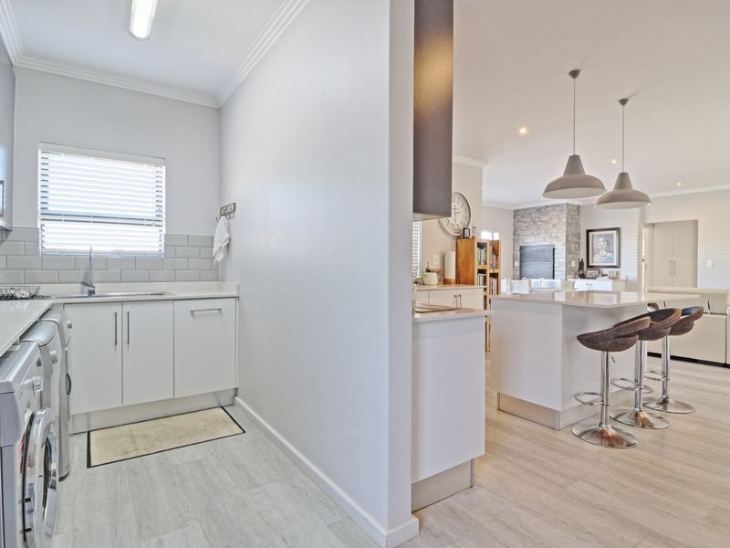 A functional scullery area featuring built-in cabinetry, subway tile backsplash, and a stainless steel sink, seamlessly connected to an open-plan kitchen and living space.