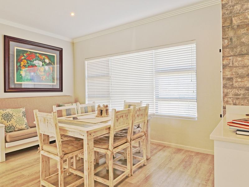 A bright dining area featuring a stone accent wall, laminate flooring, crown molding, and large windows with fitted venetian blinds.