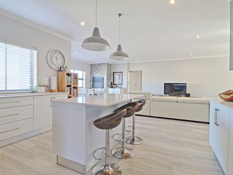Spacious open-plan living area featuring a modern kitchen with a central island, stone countertops, and a cozy built-in fireplace with stone feature wall.